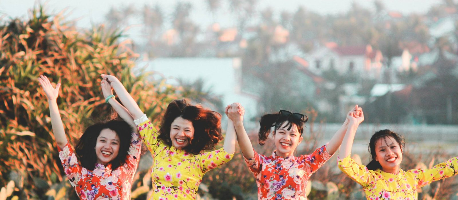 Four friends in ao dai laughing with their arms in the air