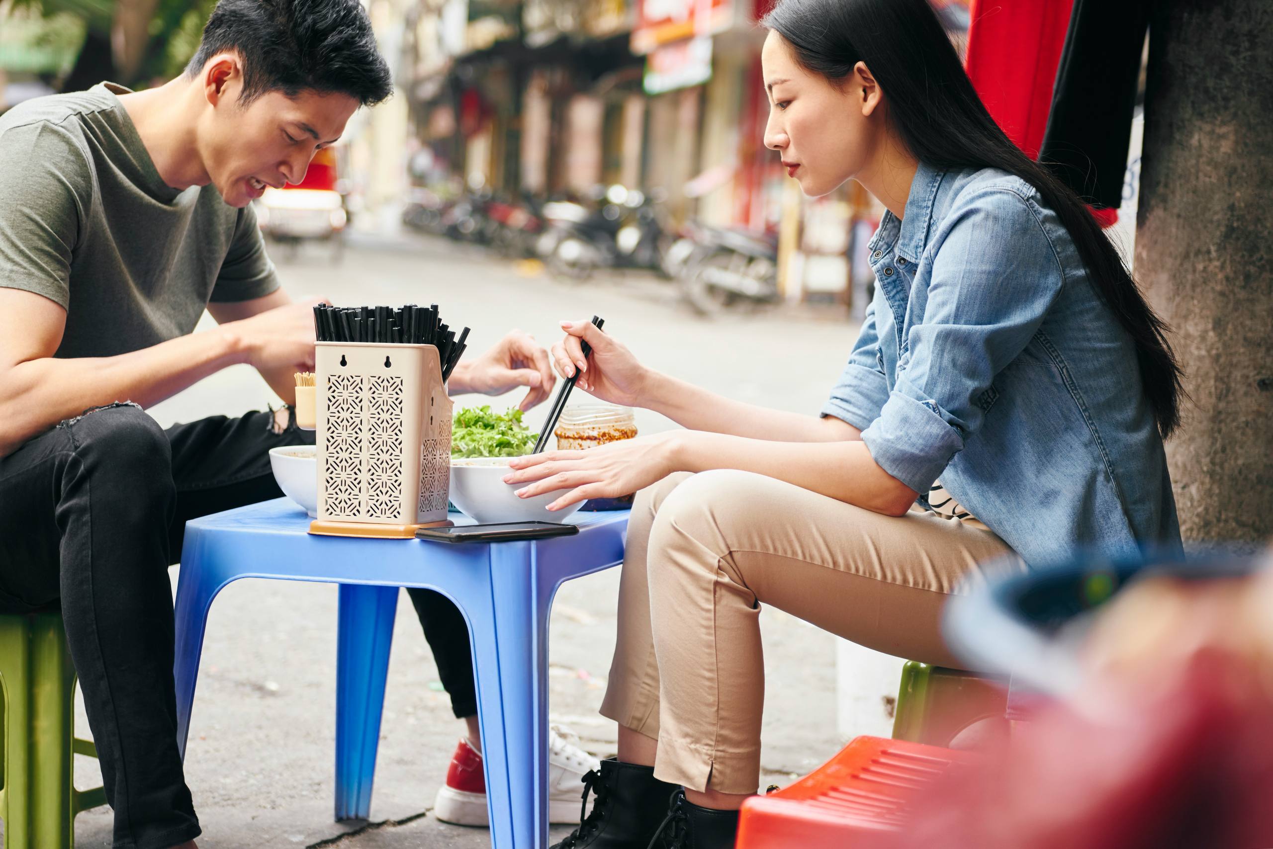 Two people sharing a bowl of noodles at a street-food table