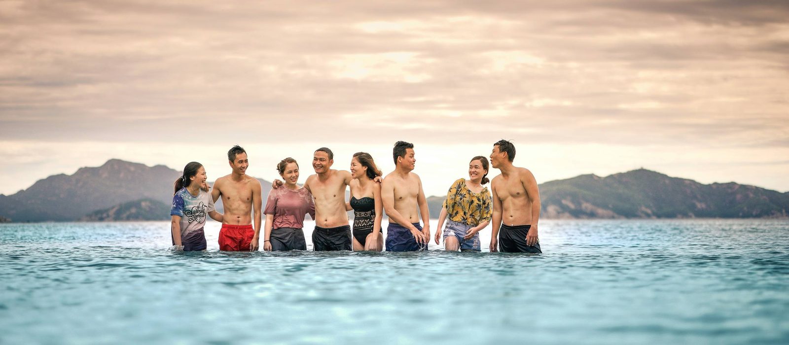 A group of friends laughing together in the sea at sunset