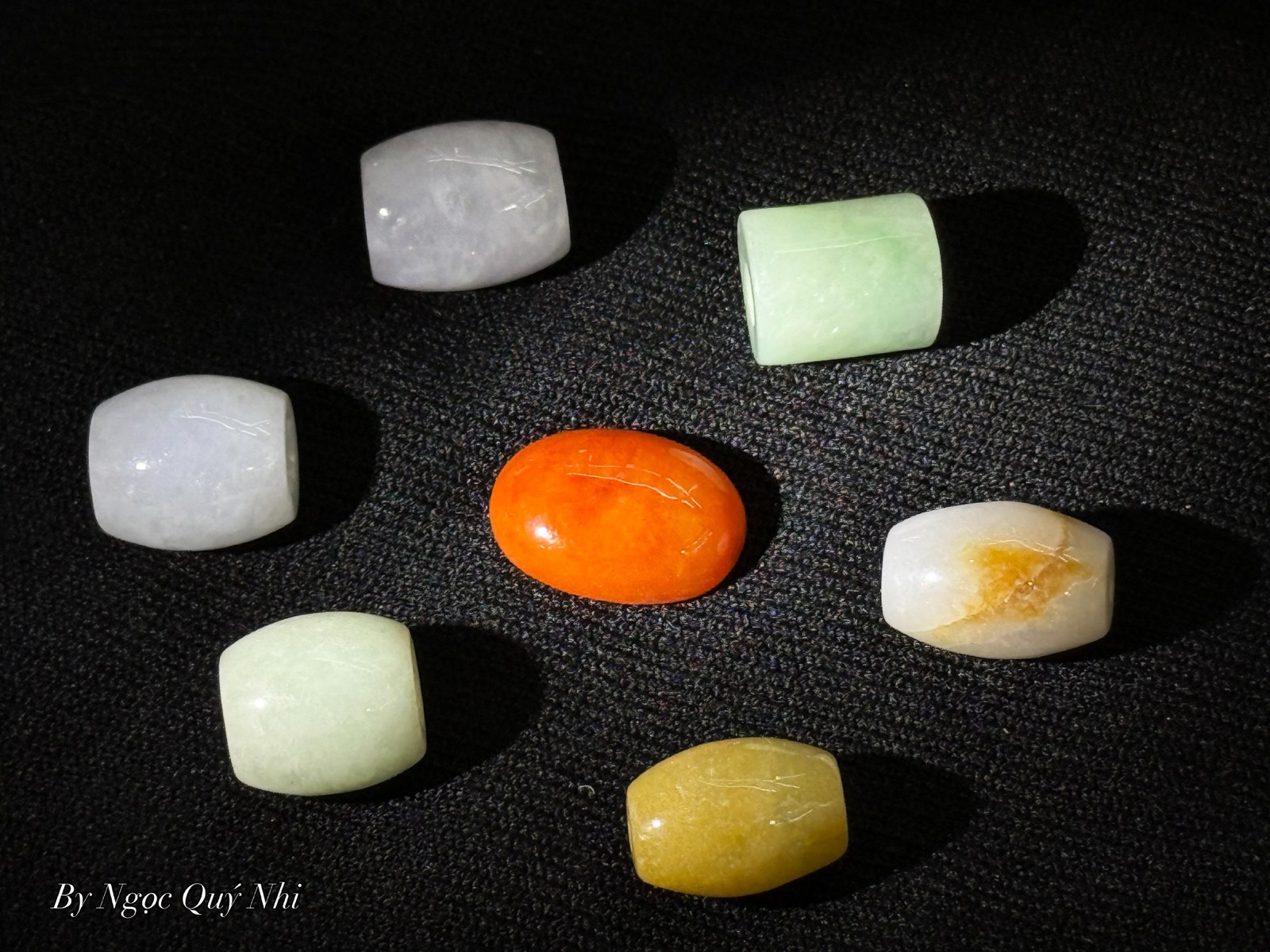 Seven polished jade and gemstone beads arranged on black cloth
