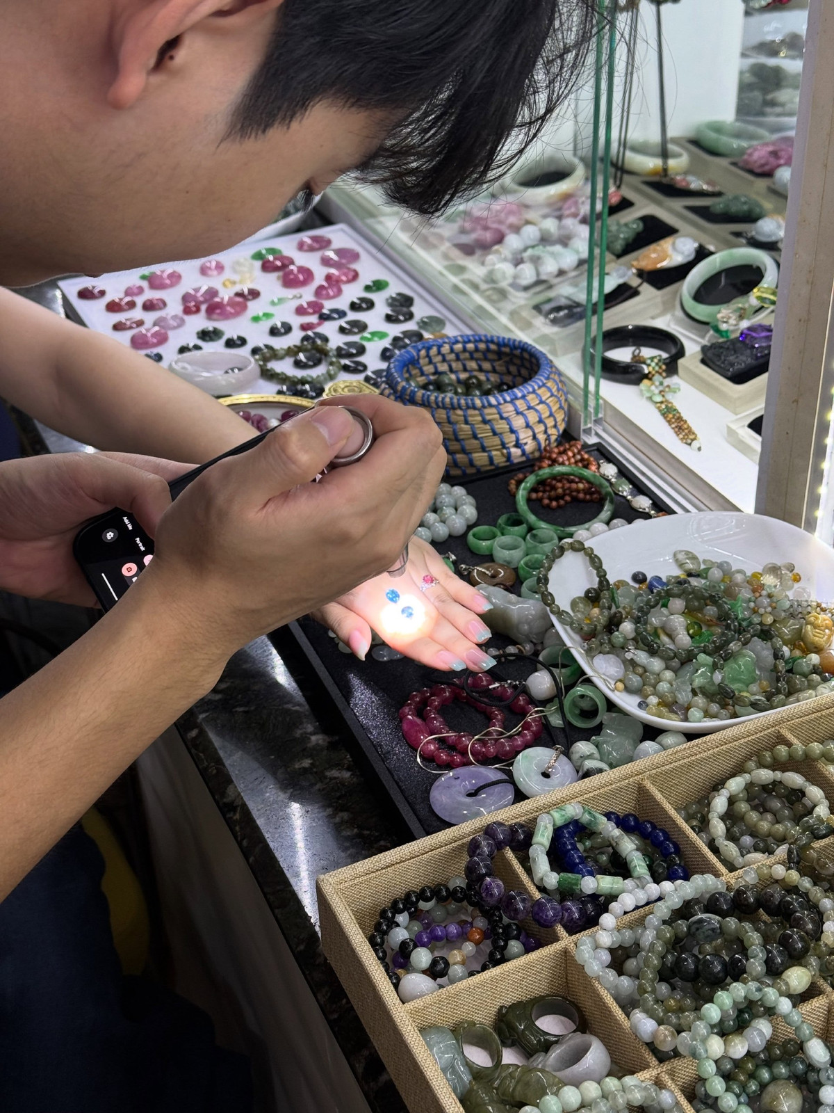 The specialist examining gemstones under a bright hand torch over trays of jade in the salon