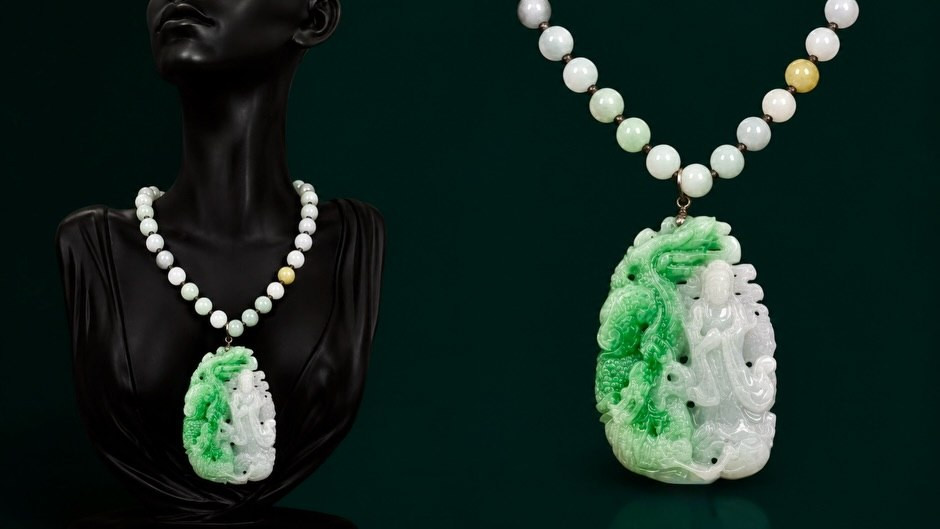 A carved jade pendant necklace displayed on a dark bust