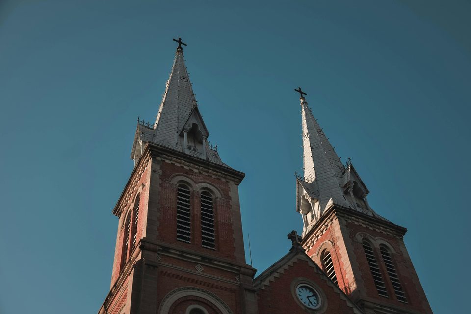 The twin red-brick spires of Notre-Dame Basilica against a clear sky, crosses at their tips and the clock face below.